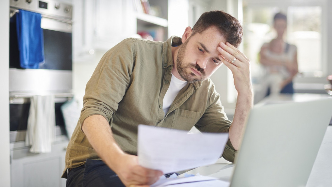 man reviewing documents are kitchen counter with open laptop