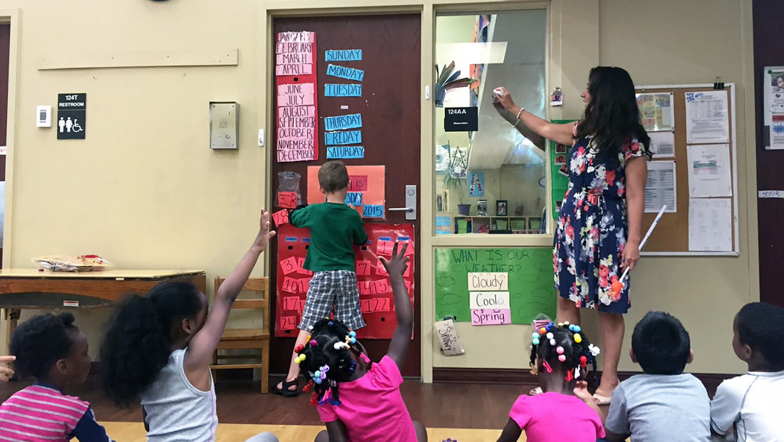 a teacher in a classroom speaking to a group of young students