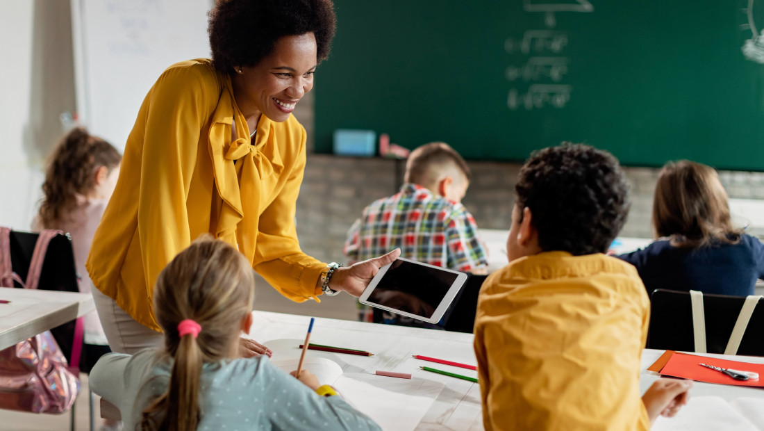 Teacher holding an iPad for a student at a classroom desk