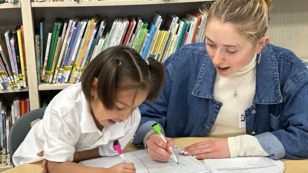 Teacher doing schoolwork with a young student at a table in the library