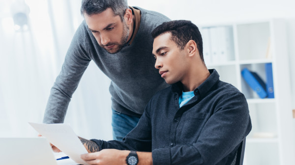 bearded-mentor-looking-at-young-colleague-working