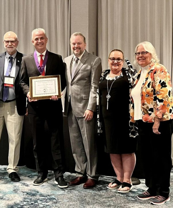 Ohio State faculty Brian Turner holding a plaque posing with a group of other Kinesiology members.
