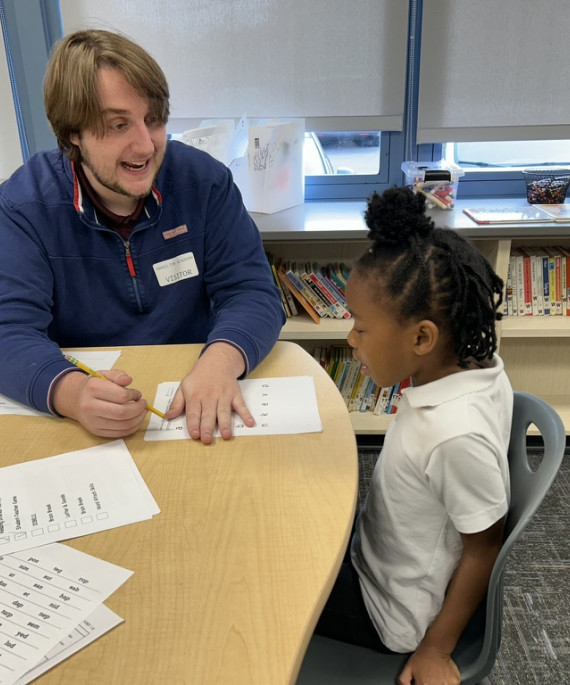 Teacher sitting at a table with young student reviewing an assignment