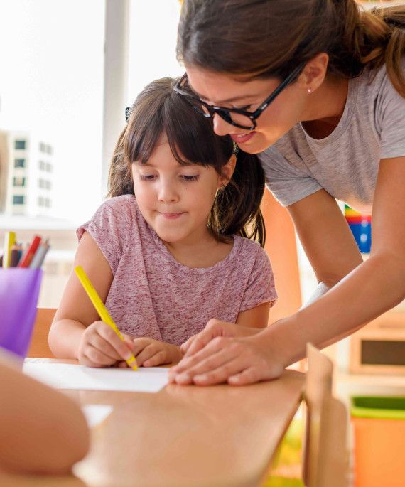 Teacher assisting a young student with a writing assignment in a classroom