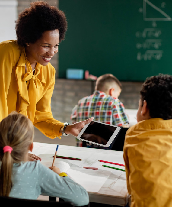 Teacher holding an iPad for a student at a classroom desk