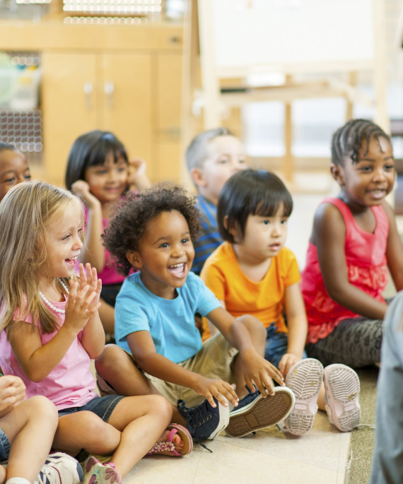 Group of kindergarten children sitting in front of a teacher reading a picture book to the class